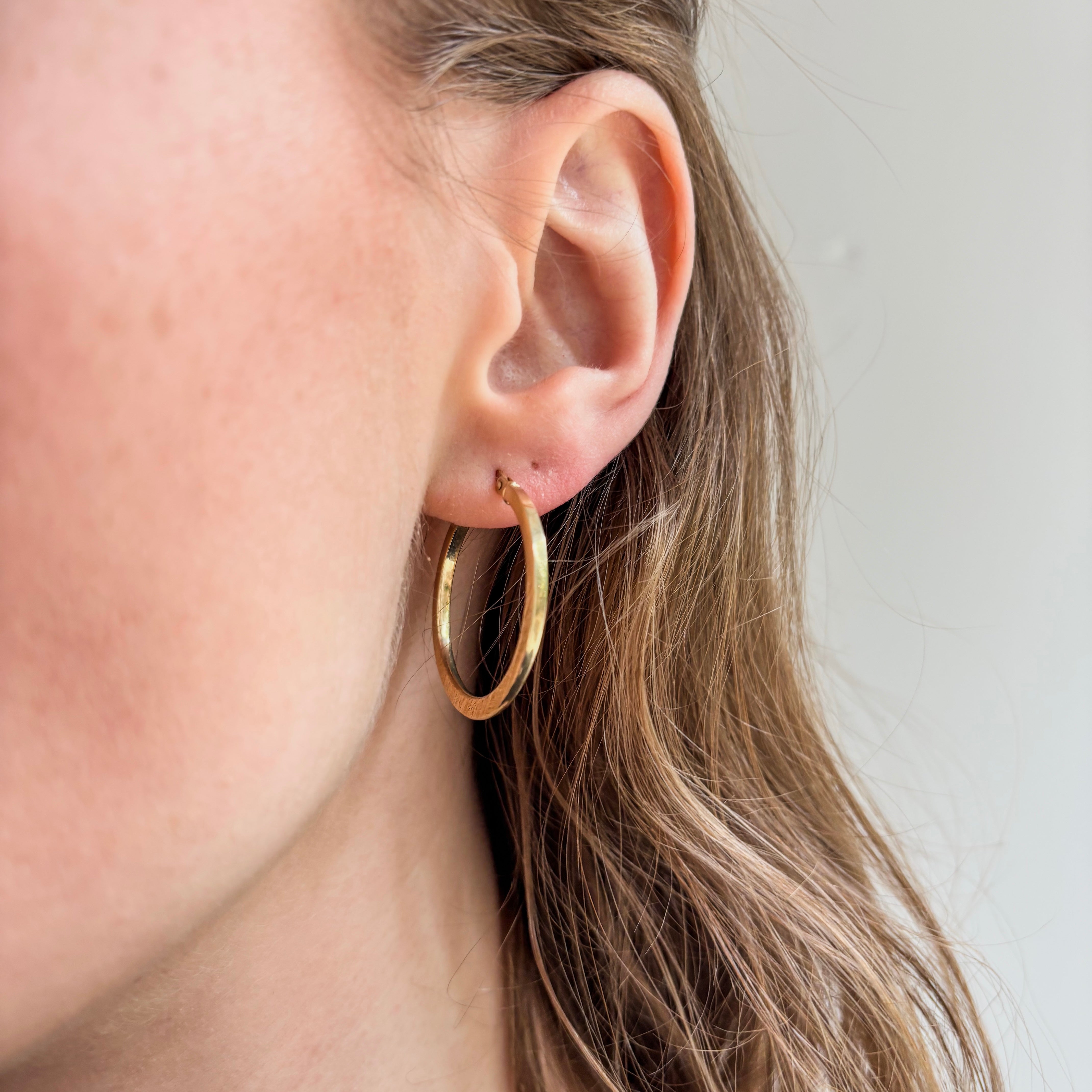 Gold hoop earring worn by a person with light skin and blonde hair.